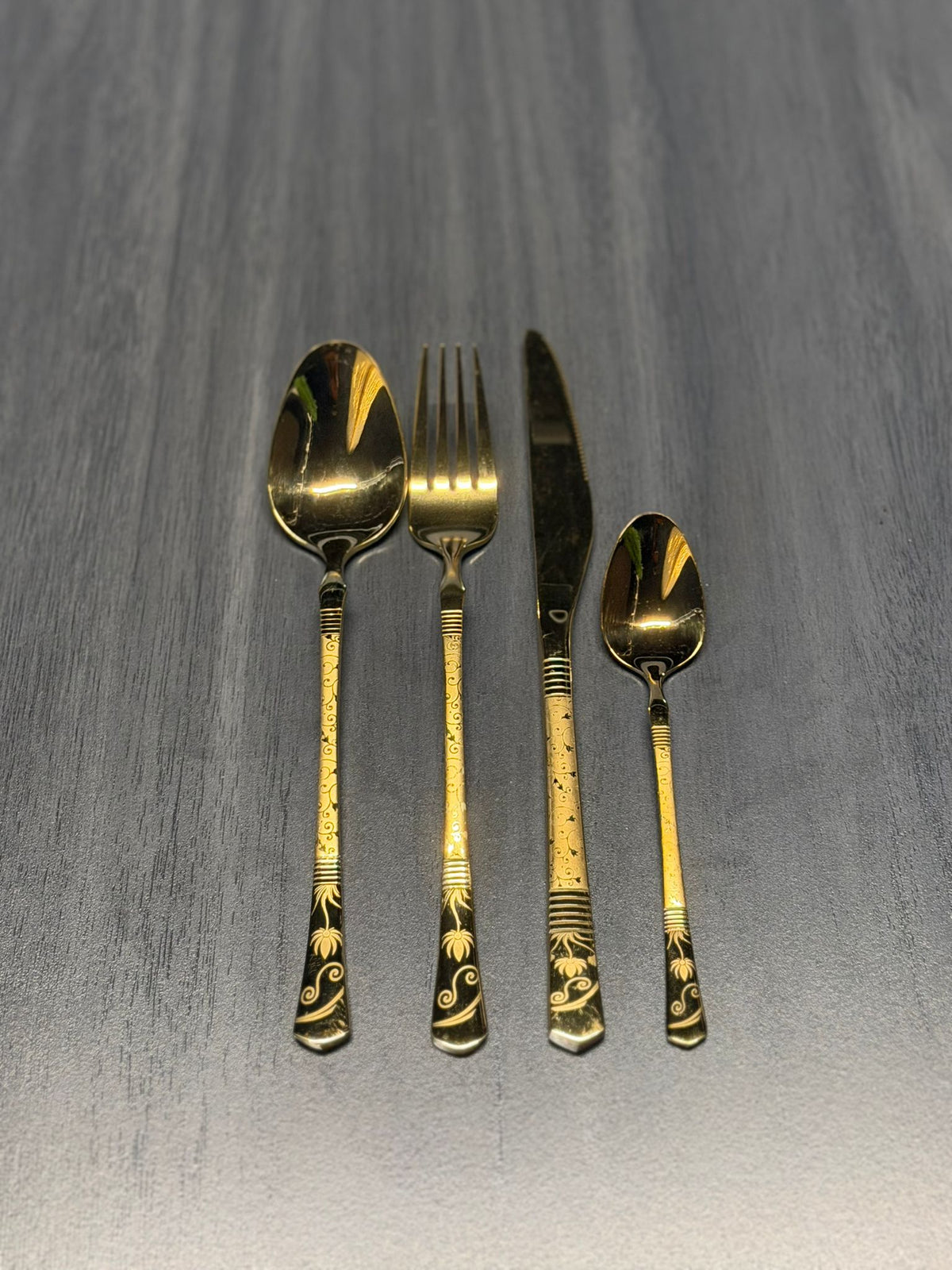 Luxury gold stainless steel cutlery set including spoon, fork, knife, and teaspoon with decorative engraved handles for catering and hospitality use.
